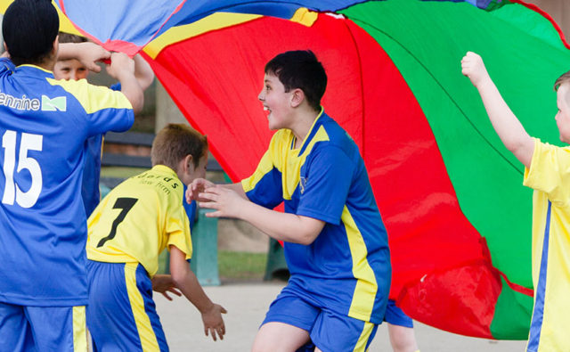 4 boys taking part in a PE lesson playing with a multi-coloured parachute