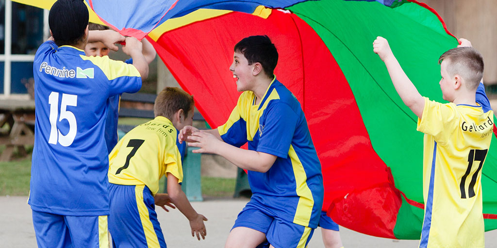 4 boys taking part in a PE lesson playing with a multi-coloured parachute