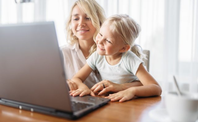 Smiling mother and child uses laptop at home